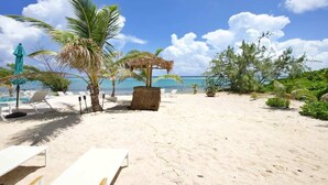 Una playa con sillones de playa, una sombrilla de paja y palmeras.