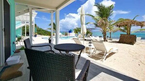 Un espacio de descanso frente a la playa con sillones de mimbre y una piscina, con vista al océano.