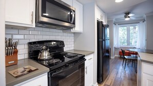 Una cocina moderna con armarios blancos, un microondas de acero inoxidable, una estufa negra y un refrigerador negro.