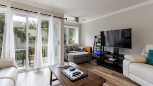 Una sala de estar con un sofá, una mesa de centro con controles remotos, un televisor y un ventanal corredera que da a un balcón.