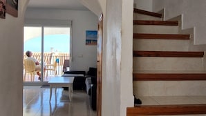 A staircase with wooden steps leading to a landing, a tiled floor, and a view of an outdoor patio area with chairs and a table.