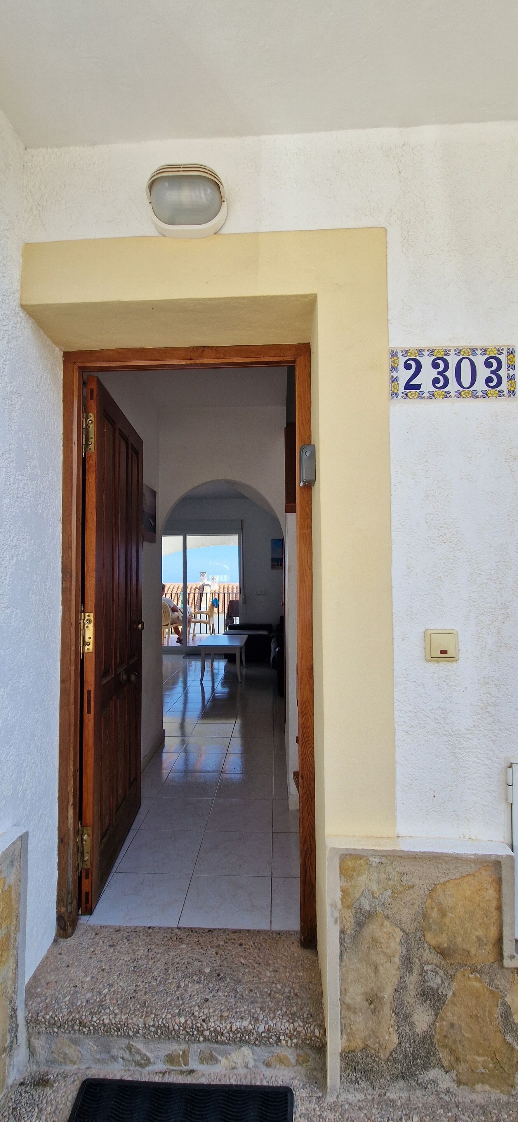 A hallway with a wooden door, a tiled floor, and a number '2303' on the wall.