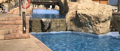 A swimming pool with a rocky edge, a no-entry sign, and a wooden bridge.