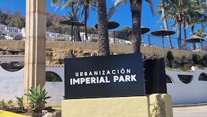 A sign for "URBANIZACIÓN IMPERIAL PARK" with palm trees and a stone column in the foreground.
