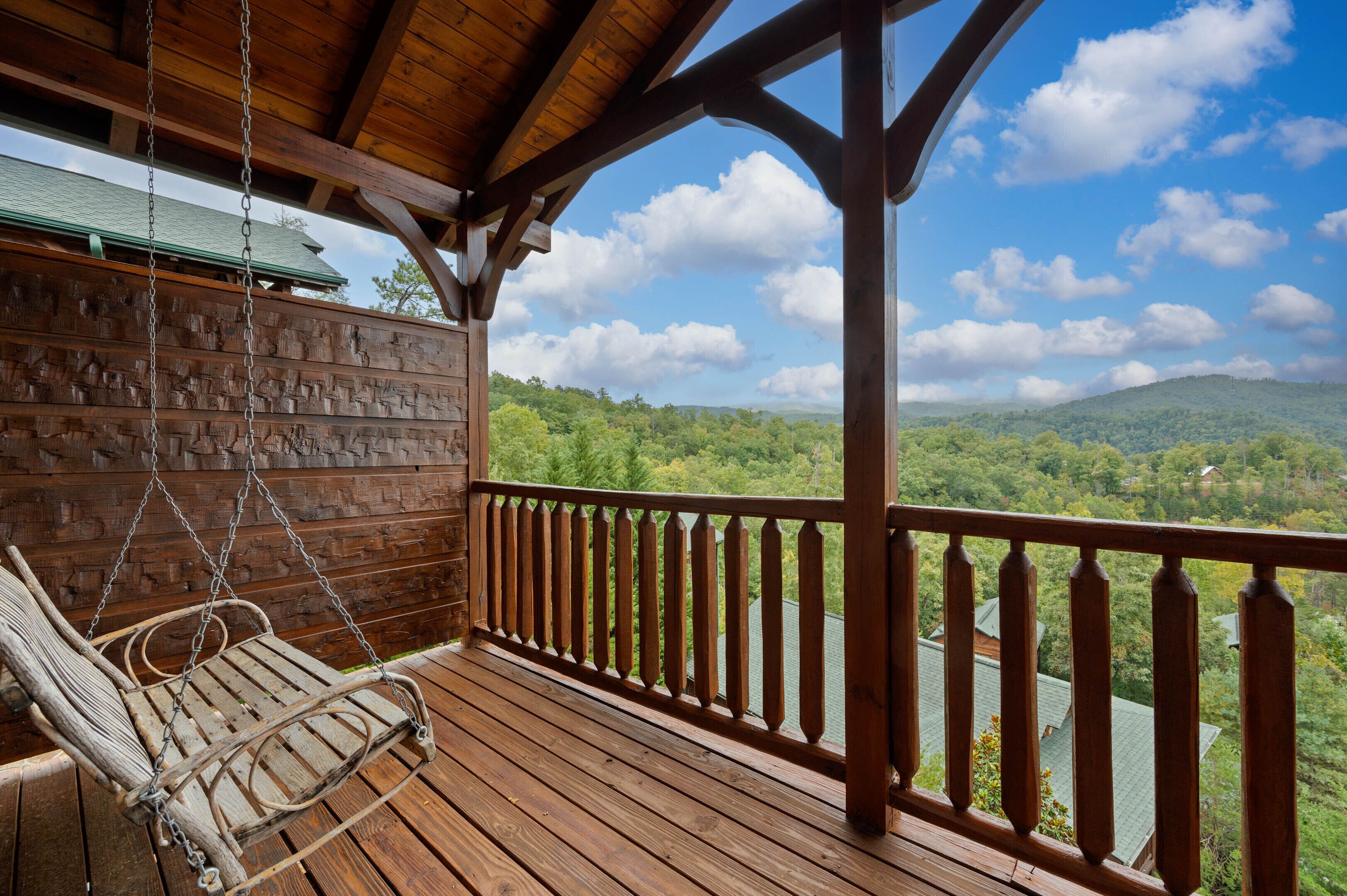 A wooden deck with a swing chair, a wooden railing, and a view of a forested landscape.