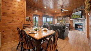 A wooden cabin interior with a dining area, fireplace, and television. - Free Tickets | Million Dollar View, Easy Access, Arcade, Fireplace, Hot Tub (Gatlinburg)