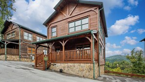A rustic wooden lodge with a stone foundation, a porch, and a scenic mountain view. - Free Tickets | Million Dollar View, Easy Access, Arcade, Fireplace, Hot Tub (Gatlinburg)