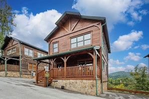 A rustic wooden lodge with a stone foundation, a porch, and a scenic mountain view.
