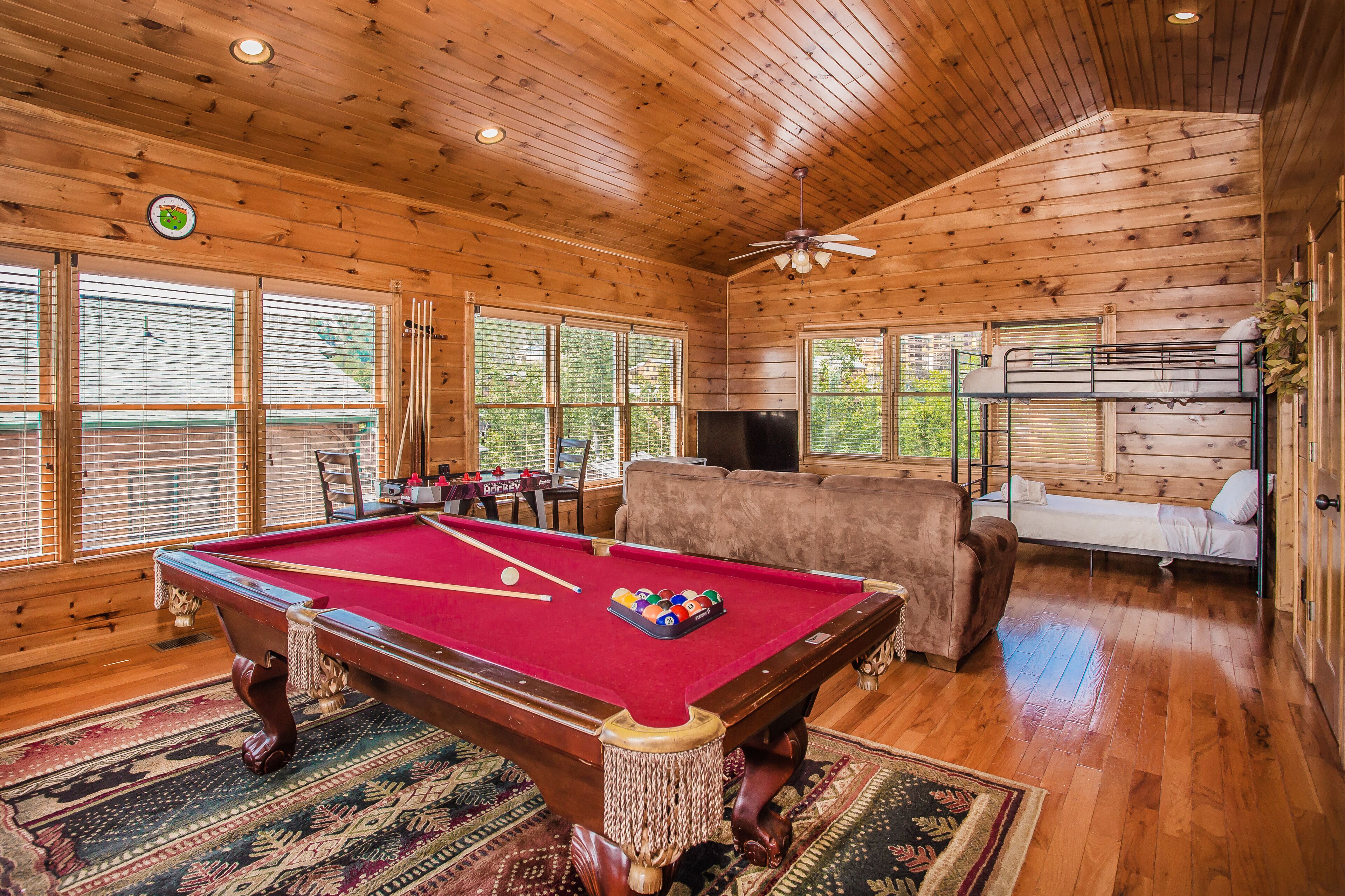 A wooden cabin with a pool table, a sofa, and a bunk bed.