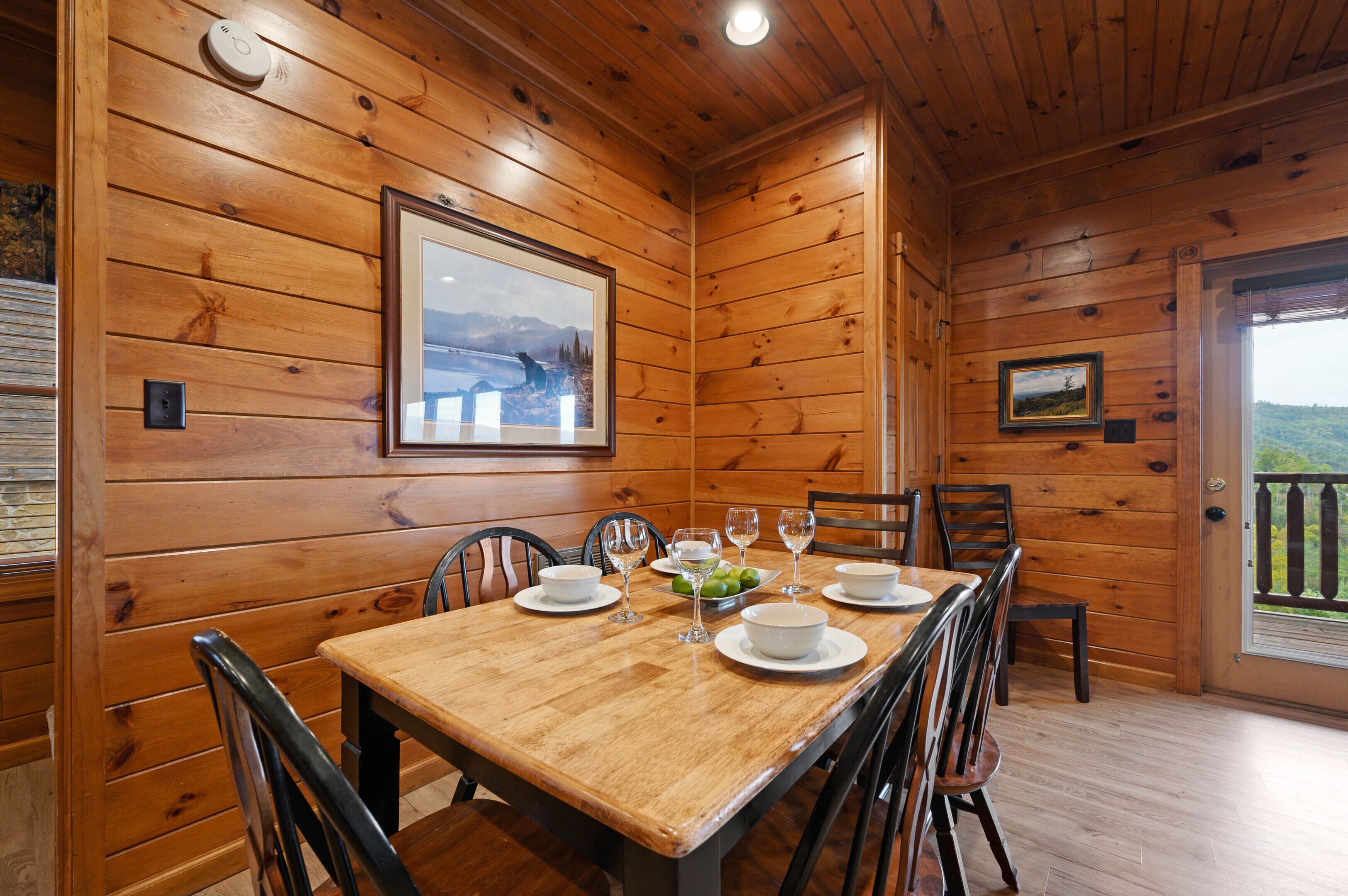 A wooden interior with a dining table set for four, chairs, and a framed picture on the wall.