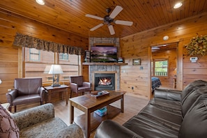 A cozy cabin interior with a fireplace, leather furniture, and a television.