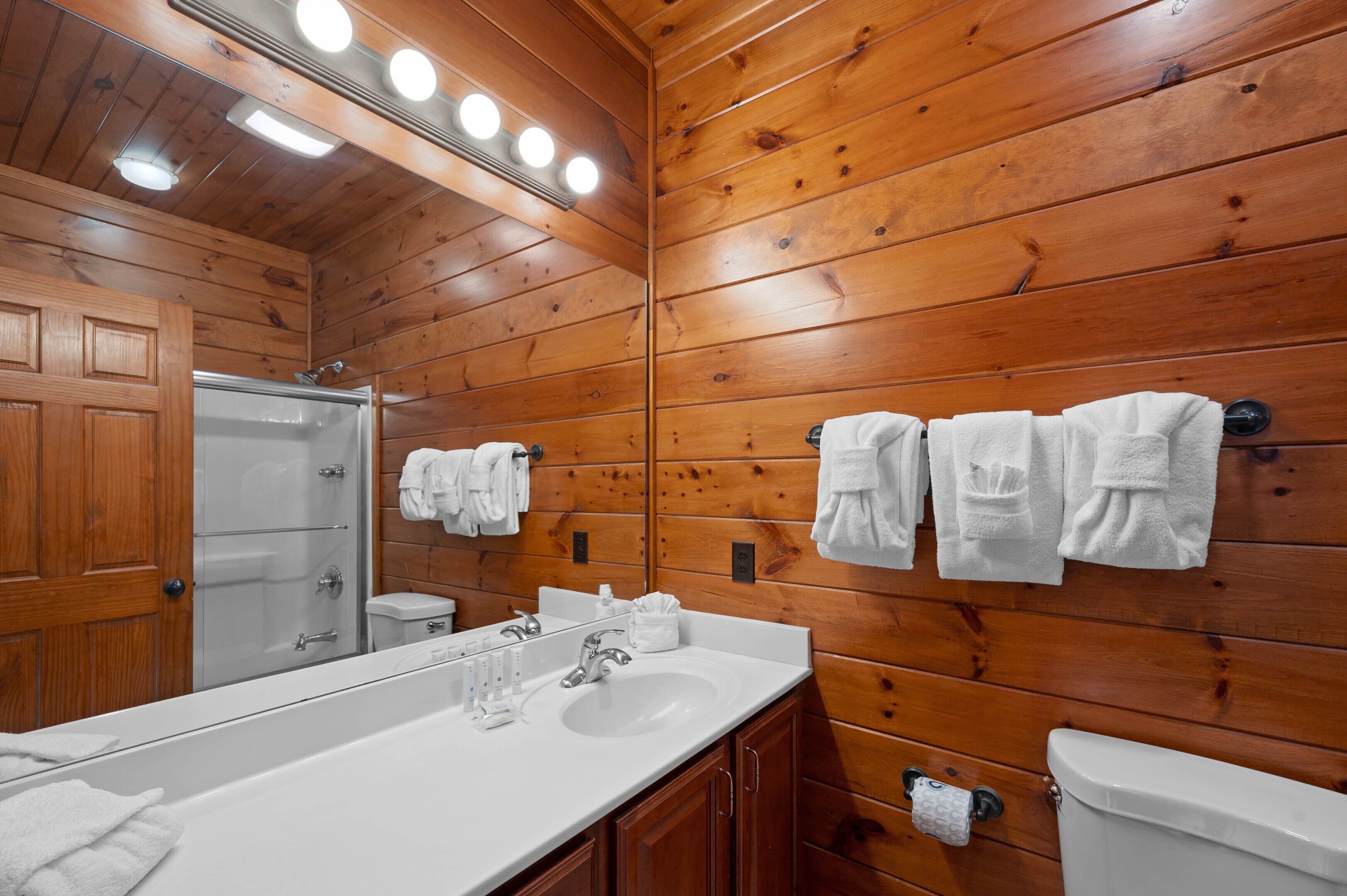 Ein Badezimmer mit Holzvertäfelung, einem großen Spiegel, einem weißen Waschbecken und zwei Toiletten.