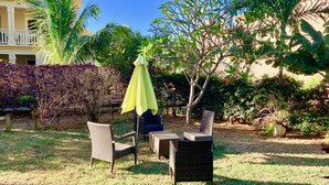 Een terras met rieten meubilair, een gele parasol en diverse planten.
