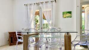 Een eethoek met een glazen tafel en stoelen, een houten kast en uitzicht op groen buiten.