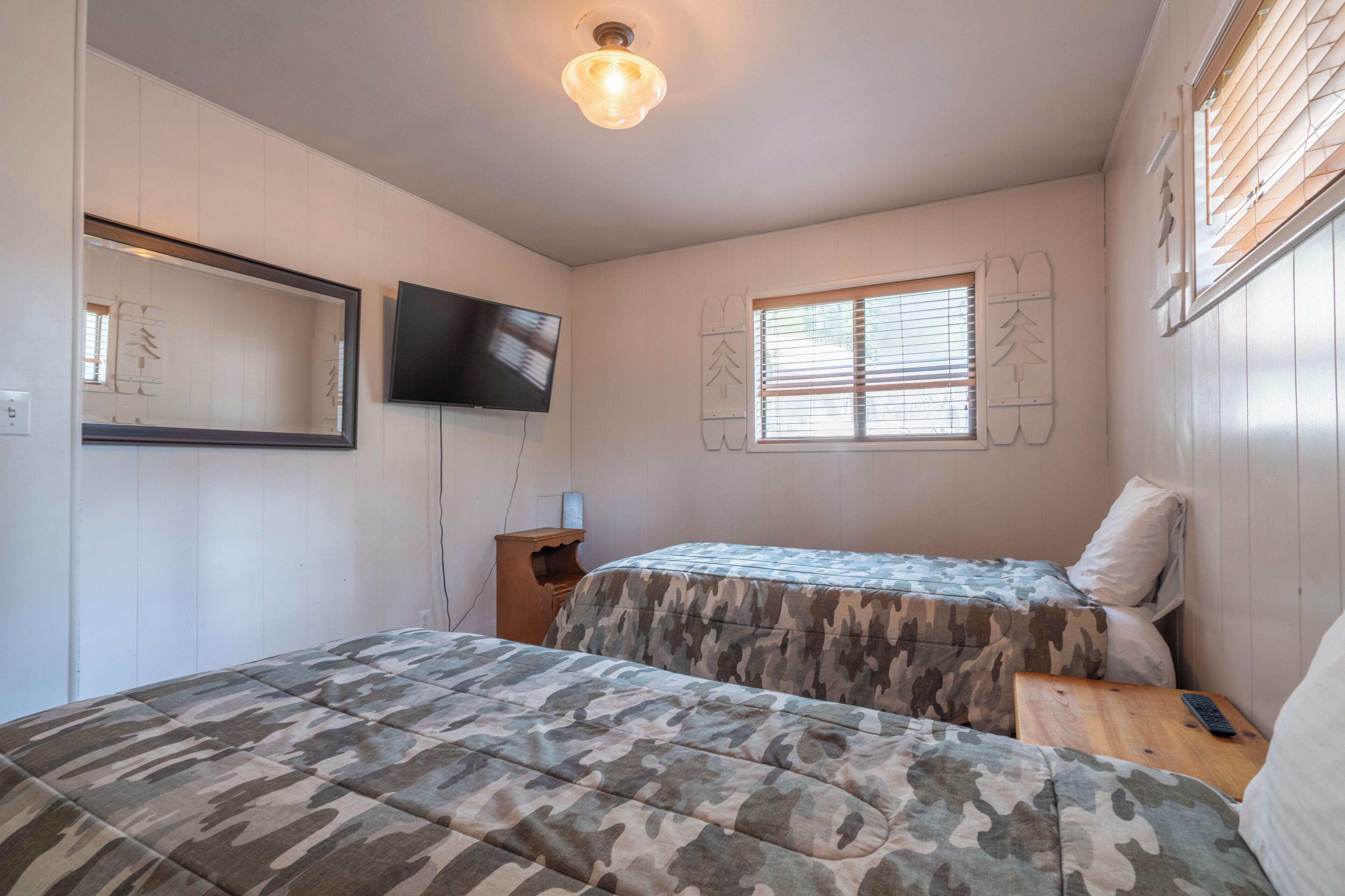 A bedroom with two beds, a TV, and a window with blinds.