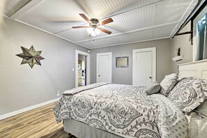 Un dormitorio con ventilador de techo, decoración de estrellas en la pared, colcha estampada y una puerta que da a otra habitación.
