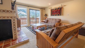 Ein Wohnzimmer mit Kamin, einer Couch, einem Couchtisch und Blick auf einen verschneiten Berg durch eine Glastür.