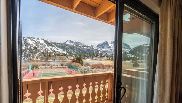 Ein Balkon mit Blick auf schneebedeckte Berge und einen Tennisplatz.