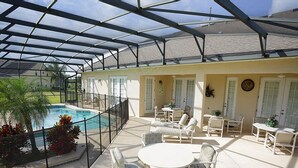 A covered outdoor area with a pool, white furniture, and a view of the pool.