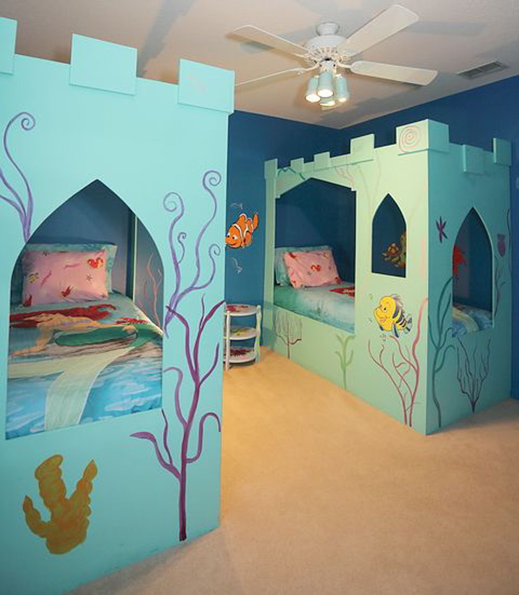 A room with three bunk beds, each with a castle-themed design, a ceiling fan, and a small table.