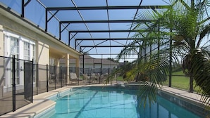 En swimmingpool med et glashegn, omgivet af palmer og en overdækket patio.