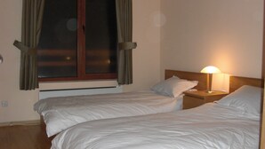 Una habitación de hotel con dos camas individuales, una mesita de noche con lámpara y un ventanal con cortinas.