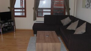 Una sala de estar con un sofá oscuro, una mesa de centro de madera y un televisor sobre un mueble.