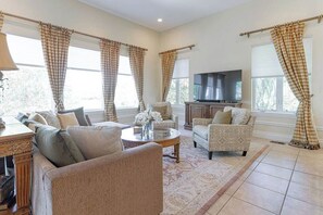 A living room with a sofa, armchairs, a coffee table, a TV, and curtains.