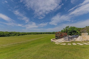 Eine grüne Wiese mit einer Terrassenfläche und Gartenmöbeln.