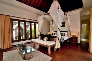 A bedroom with a canopy bed, a glass coffee table, and a view of greenery through large windows. - The ultimate Bali beachside getaway at Villa Kaira Estate, a 7-bedroom luxury villa in Berawa, Canggu. The Estate offers daily breakfast, a full-time private chef, airport transfers, complimentary massages, housekeeping, and a dedicated driver. (North Kuta)