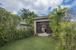 Une maison traditionnelle avec un portail en bois, une pelouse bien entretenue et une végétation tropicale luxuriante.