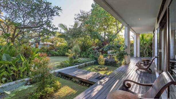 A wooden deck with a bench and table, surrounded by lush greenery and a garden. - The ultimate Bali beachside getaway at Villa Kaira Estate, a 7-bedroom luxury villa in Berawa, Canggu. The Estate offers daily breakfast, a full-time private chef, airport transfers, complimentary massages, housekeeping, and a dedicated driver. (North Kuta)