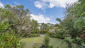 A lush garden with a variety of plants and a stone pathway leading to a building. - The ultimate Bali beachside getaway at Villa Kaira Estate, a 7-bedroom luxury villa in Berawa, Canggu. The Estate offers daily breakfast, a full-time private chef, airport transfers, complimentary massages, housekeeping, and a dedicated driver. (North Kuta)