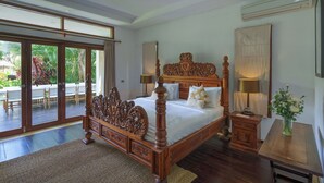 A spacious bedroom with a large bed, a wooden nightstand, a small table, and a view of a patio with outdoor furniture. - The ultimate Bali beachside getaway at Villa Kaira Estate, a 7-bedroom luxury villa in Berawa, Canggu. The Estate offers daily breakfast, a full-time private chef, airport transfers, complimentary massages, housekeeping, and a dedicated driver. (North Kuta)