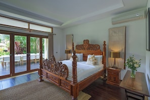 A spacious bedroom with a large bed, a wooden nightstand, a small table, and a view of a patio with outdoor furniture.