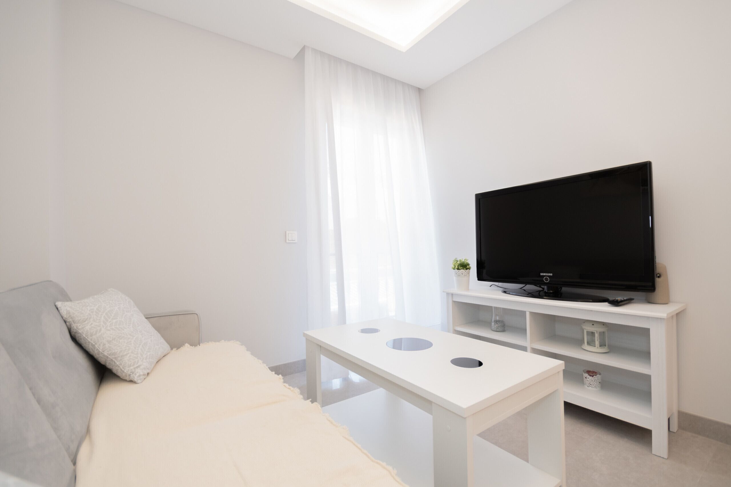 A modern living room with a sofa, a TV on a white stand, and a small table.
