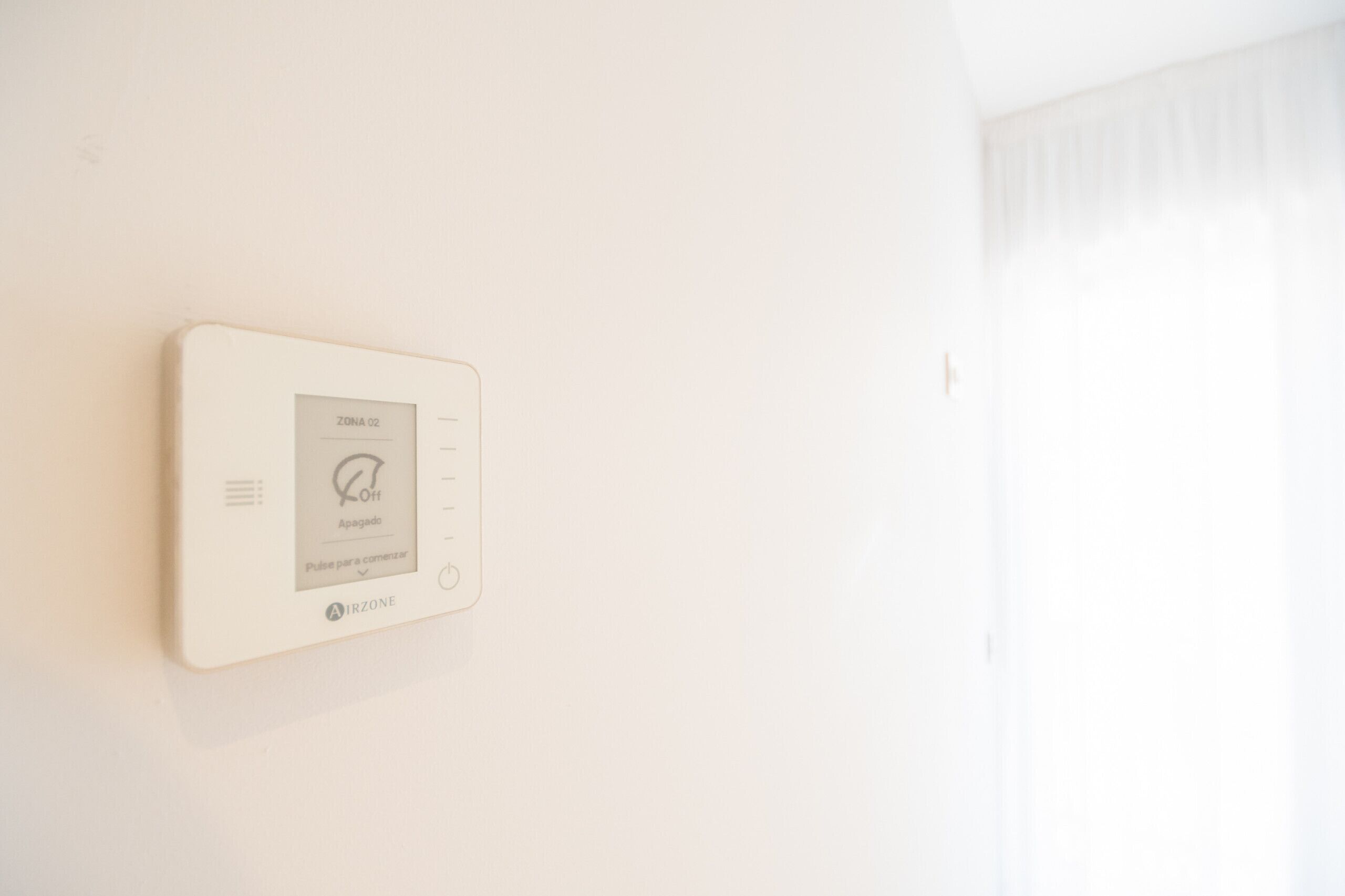 A wall-mounted thermostat with a digital display, indicating a temperature setting and a power button.