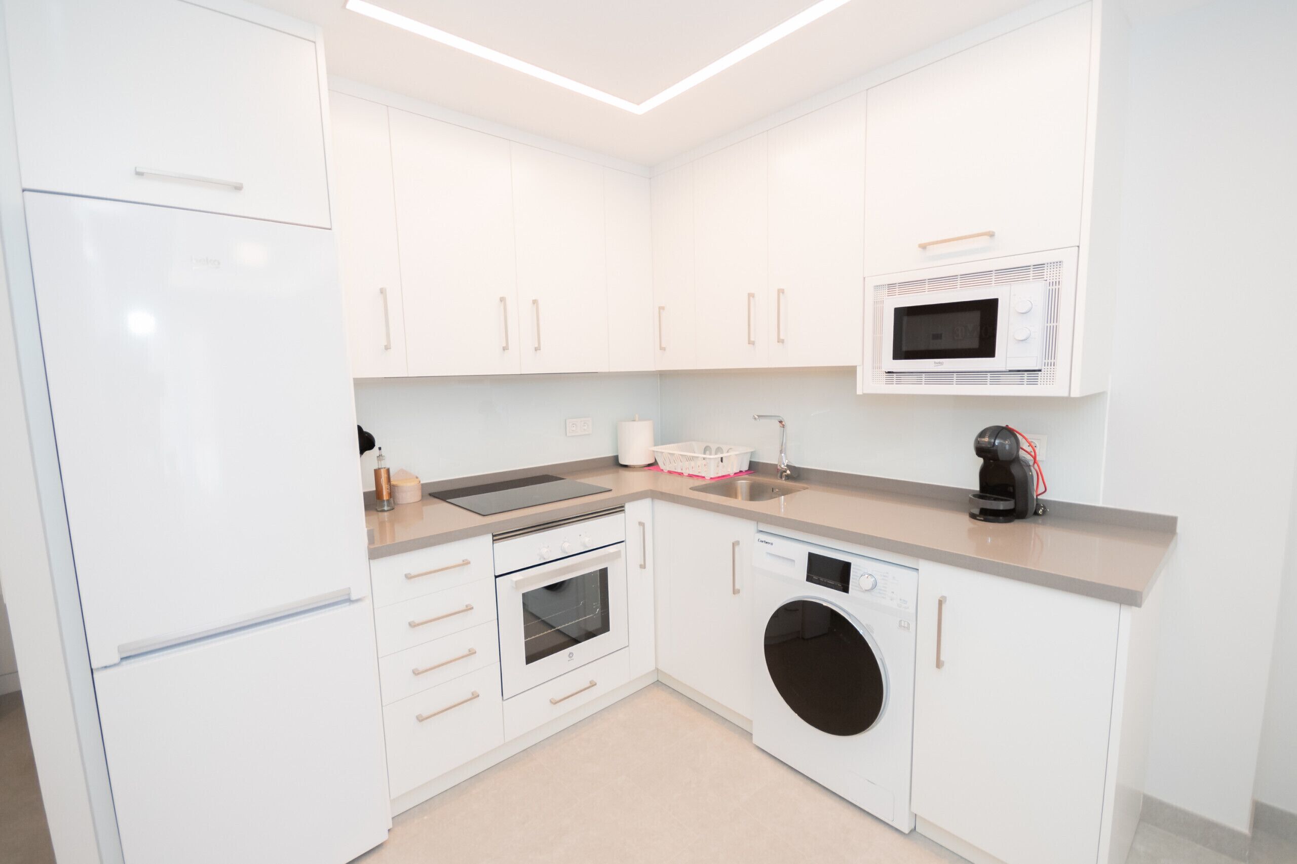A modern kitchen with white cabinetry, a built-in oven, microwave, and dishwasher.