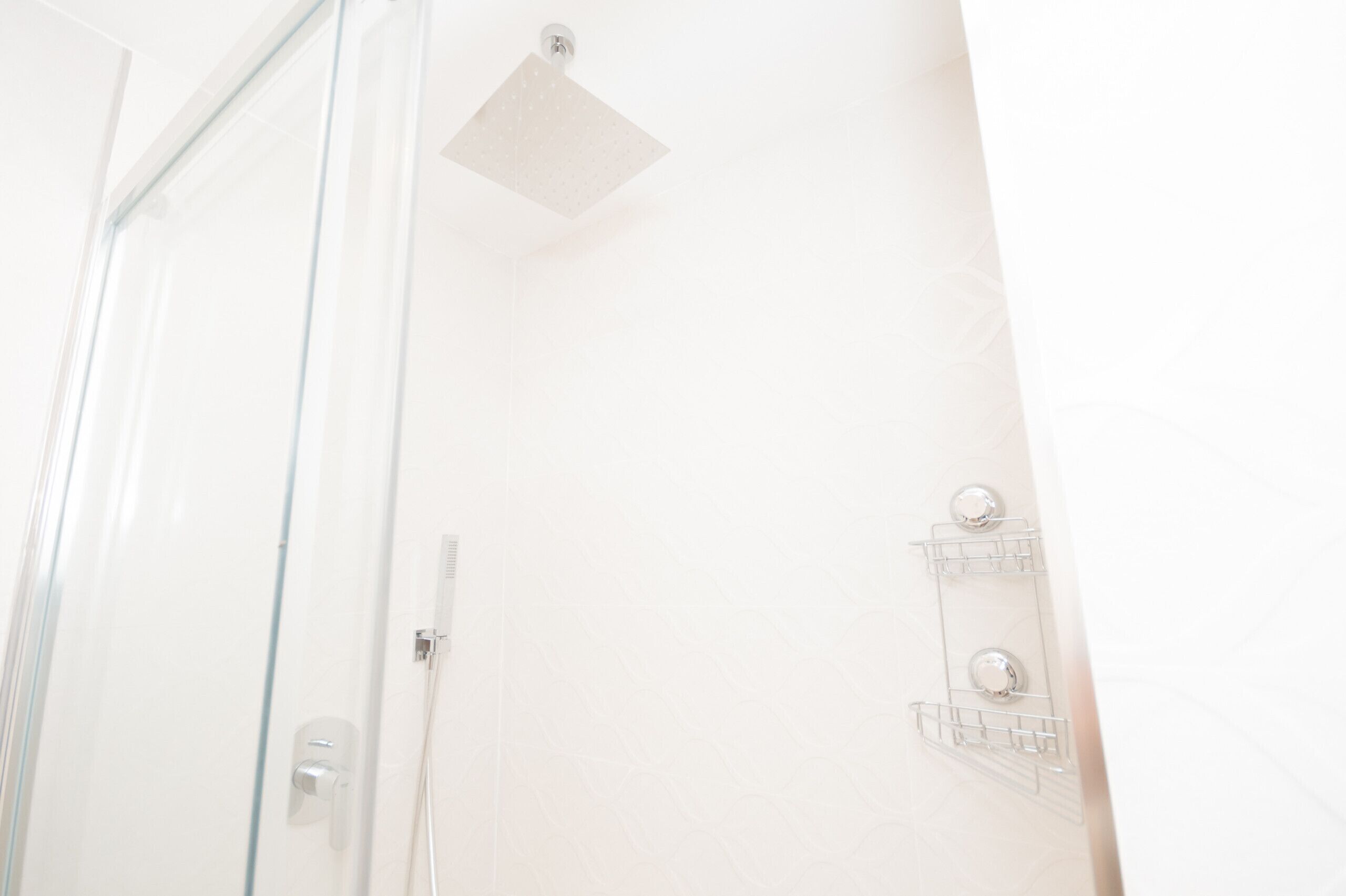 Een badkamer met een douchecabine van glas, een witte betegelde muur en een douchekop.