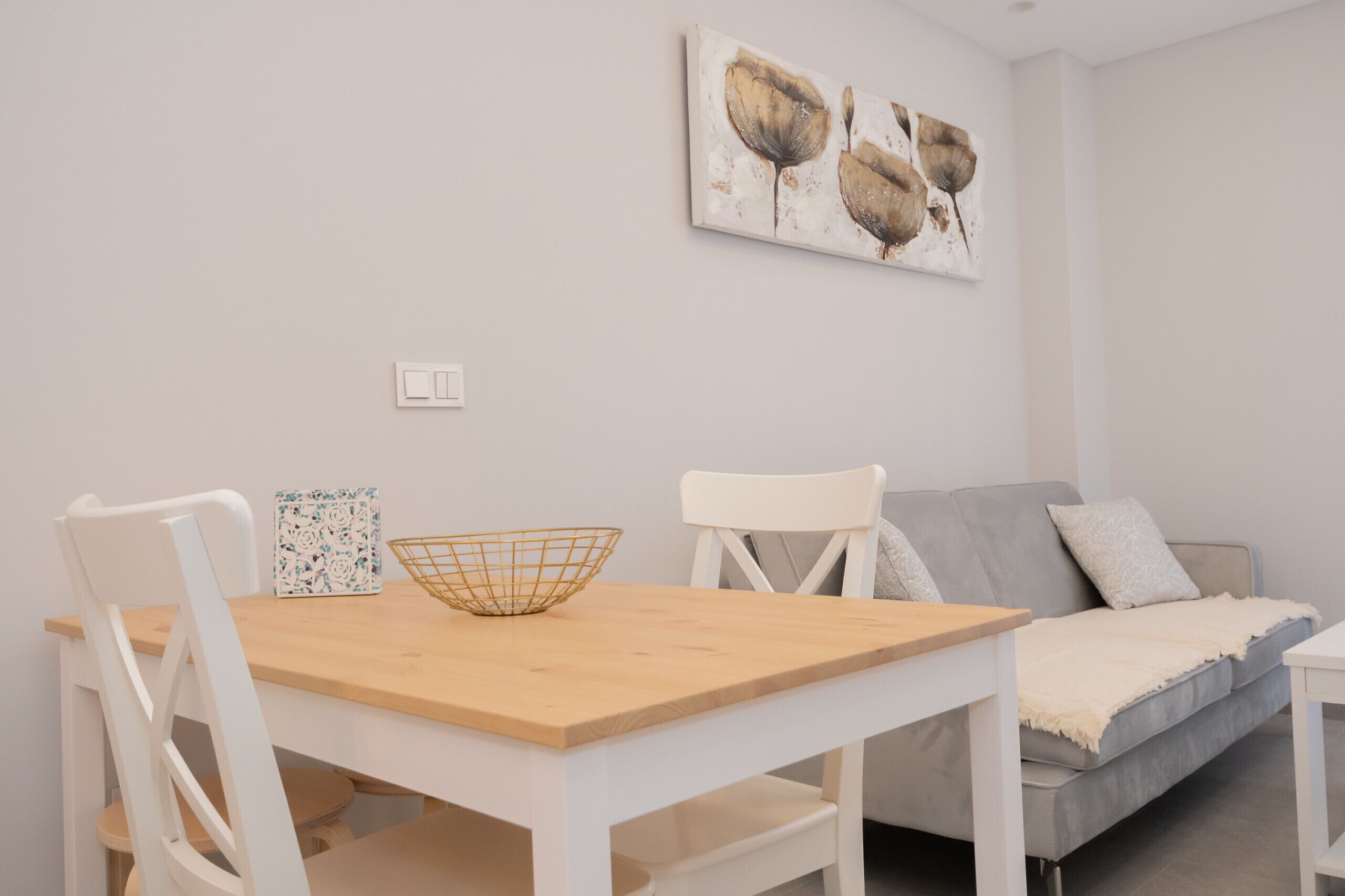 Een eetgedeelte met een houten tafel, witte stoelen, een witte bank en een schilderij dat aan de muur hangt.