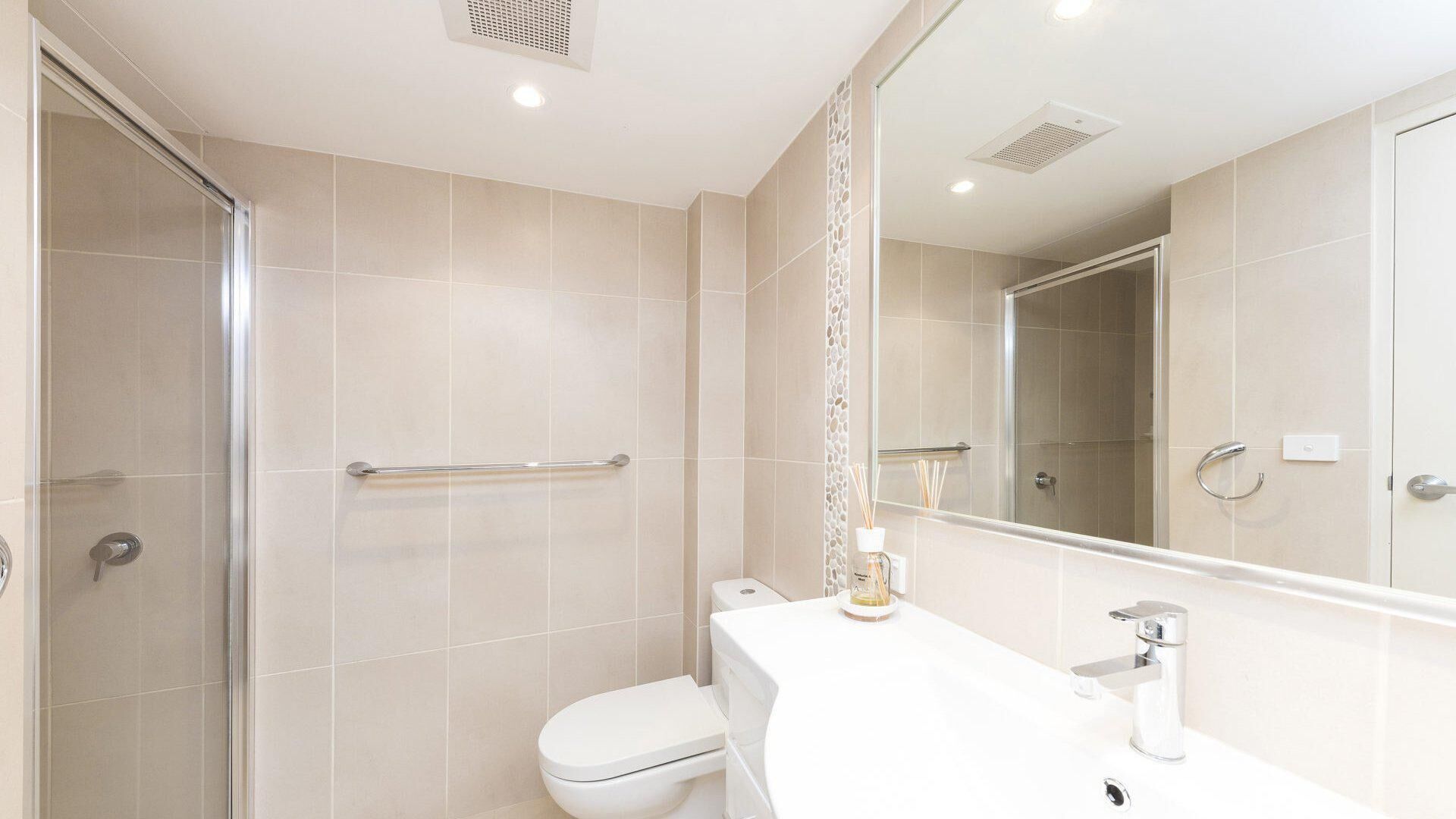 A modern bathroom with a glass shower enclosure, a white toilet, and a vanity with a mirror.