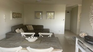 A living room with a sofa, a dining table with chairs, and a kitchen area with a refrigerator. - Newly Renovated Unit near Forster Main Beach! (Forster)