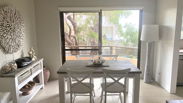 A dining area with a table and chairs, a decorative wall piece, and a view of the outdoors. - Newly Renovated Unit near Forster Main Beach! (Forster)