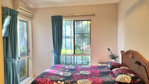 A bedroom with a bed, a window with curtains, a bedside table, and a lamp.