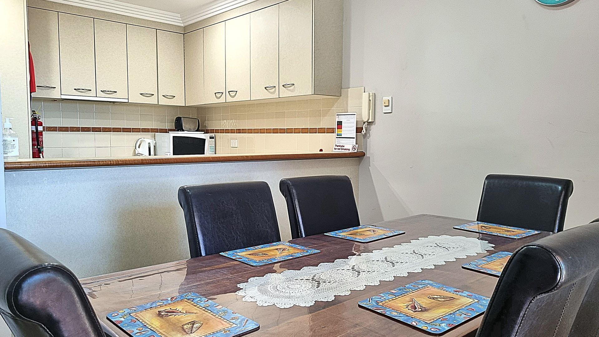 A dining area with a wooden table, four chairs, and a lace table runner.