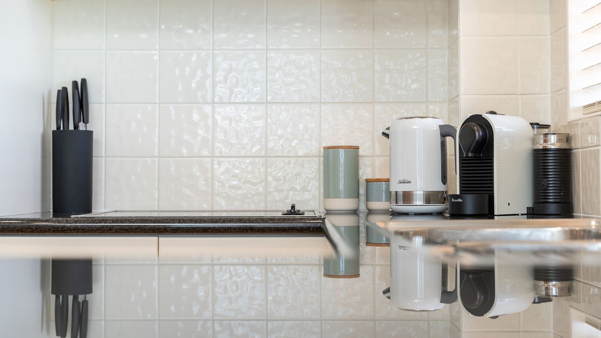 Eine Küche mit weißen Fliesen, einer Kaffeemaschine, einem Wasserkocher und einer Breville-Kaffeemaschine.