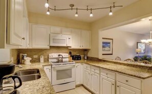A kitchen with white cabinets, a stove, a coffee maker, and a sink.