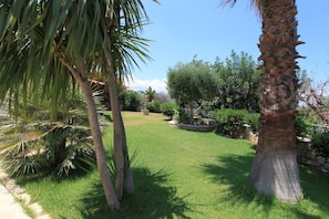 Un jardin bien entretenu, avec une variété d’arbres, notamment des palmiers, et une pelouse soigneusement taillée.