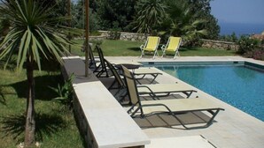 A poolside area with lounge chairs, a palm tree, and a view of the ocean. - Villa Persephone, drofnah and beach (Rethymnon)