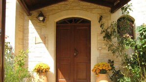 A stone building with a wooden door, two large flower pots with yellow flowers, and climbing plants on the right. - Villa Persephone, drofnah and beach (Rethymnon)